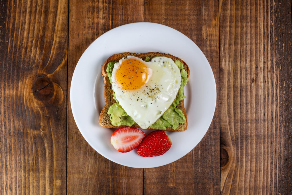 Toast with avocado and egg with heart shape  on white plate