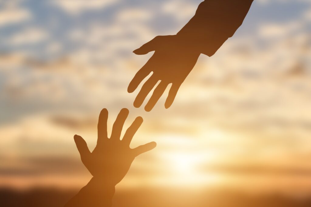 Silhouette of giving a helping hand, hope and support each other over sunset background.